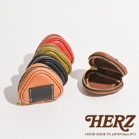 職人手作皮革小物收納包，共五色：橘棕、黑、墨綠、紅、咖其色。設計成三角飯糰造型，採用拉鍊開合，材質為皮革。其中一個收納包打開展示內部。