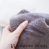 野村毛巾 YABAI 水漾瞬吸厲害毛巾，手觸灰色毛巾，上面有 NOMURA TOWEL 字樣。