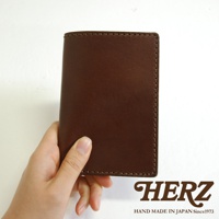 手持深棕色皮革護照套，表面有精緻縫線，質感樸實。