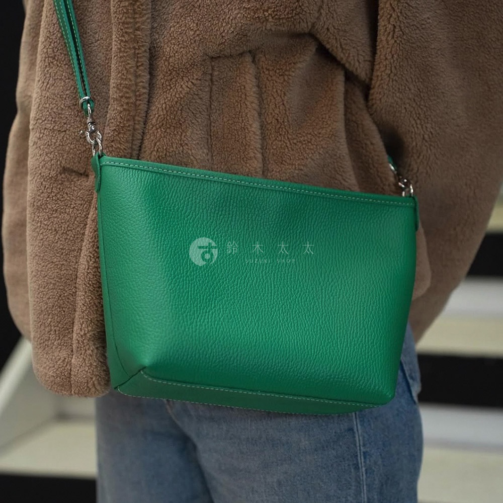 綠色皮革製成的長方形隨身側背包，帶有可調節的細長肩帶和銀色金屬扣環。包身縫線明顯，表面帶有細緻的紋理。
