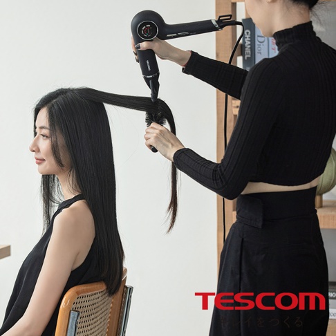 一位髮型師正在使用吹風機和梳子為一位女性吹乾頭髮，品牌 TESCOM 標誌在右下角
