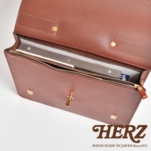 棕色皮革製成的商務公事包，打開的包蓋露出內部，可見拉鍊開合，包包正面有金屬鎖扣和兩個金屬釘。