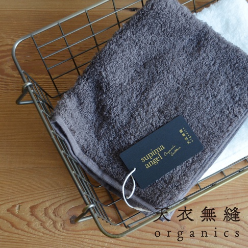 金屬籃子內放著一條深灰色、蓬鬆柔軟的匹馬棉毛巾，旁邊疊著一條白色毛巾。毛巾上有一個黑色吊牌，印有金色「supima angel Organic Cotton」字樣。