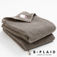 疊放的 EVE 今治製大浴巾，呈現深棕色，表面有細緻的鱗紋織法，質料厚實，一角的織標標示著品牌名稱「B-PLAID」及「MADE in JAPAN」。