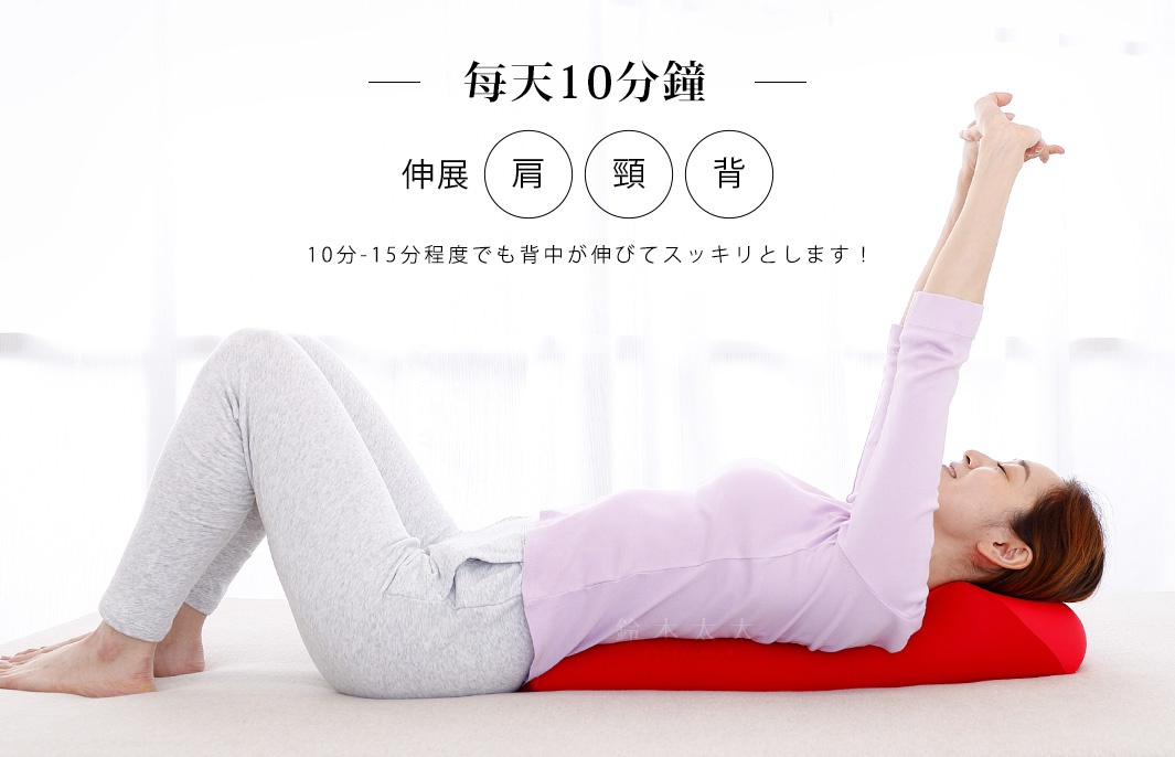 一位女士躺在紅色的舒背拉伸枕上，雙手舉過頭頂伸展。拉伸枕為圓柱形，表面光滑，材質看起來柔軟。