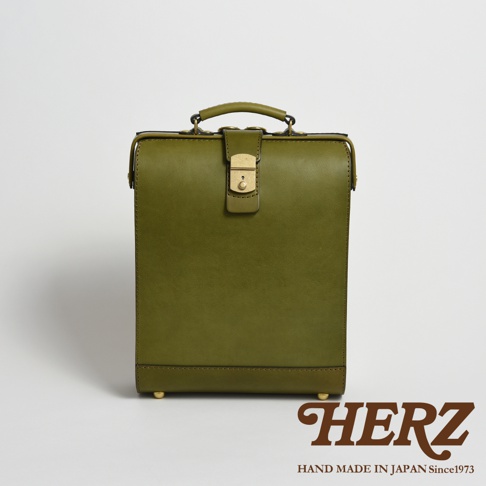 橄欖綠皮革製成的職人手作杜勒斯商務後背包，正面有一個金色旋鈕鎖扣及提把，底部有四個金屬腳釘，風格簡潔復古。