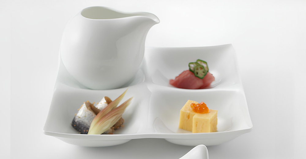 白色陶瓷三格小菜盤，配有醬汁壺，盤中盛有生魚片佐秋葵、烤魚佐薑芽，以及玉子燒佐鮭魚卵。