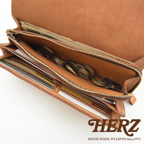 職人手作皮革長夾，展示其手風琴式多卡層設計，內部裝有鈔票與硬幣。皮革呈現自然棕色，配有黃銅色拉鍊。