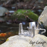 銀色不鏽鋼伸縮式瀝水架，結構層疊，附帶一個銀色不鏽鋼杯和夾子，置於岩石上，背景是溪流與綠色植被。