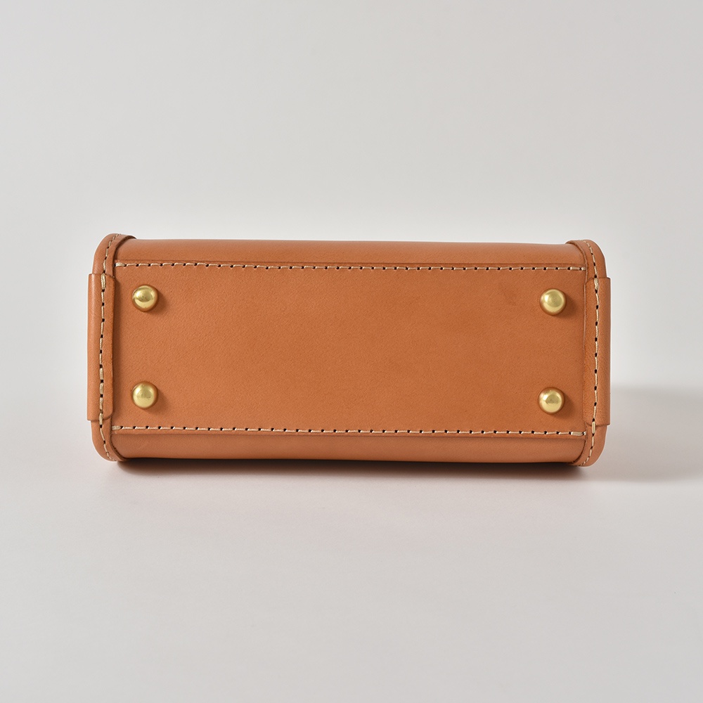 職人手作皮革單肩兩用拱型手袋 Q-16，展示為焦糖棕色，採用光滑皮革製成，包身側面有雙排縫線裝飾，底部設有四個金色圓形金屬腳釘，提供四種顏色選擇。