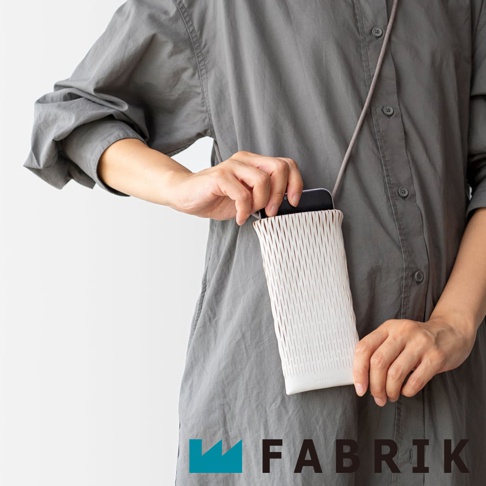 FABRIK 品牌標誌旁，一位身穿灰色襯衫的人正將一支手機放入白色網狀材質的長形側背包中。