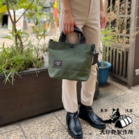 綠色帆布材質的兩用托特包，有黑色提把與可拆卸斜背帶，包身正面有兩個方形布貼，其中一個印有黑犬圖案。