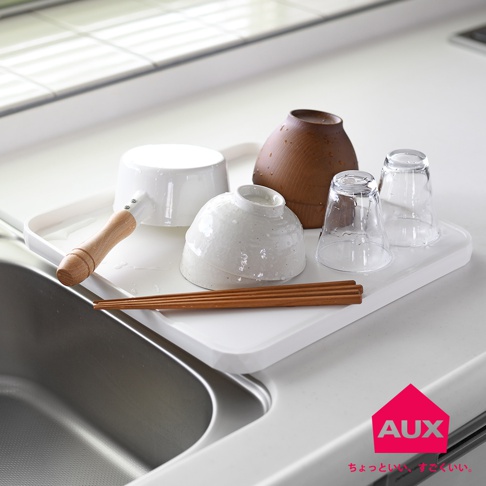 白色塑膠瀝水盤上，擺放著一個附木質把手的白色陶瓷鍋，一個粗糙紋理的白色陶瓷碗，一個深棕色木碗，兩個透明玻璃杯，以及一雙木筷。