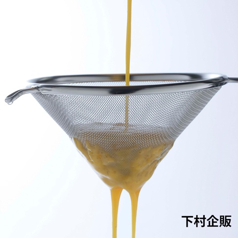 不鏽鋼錐型濾網，網目細緻，用於過濾黃色液體，濾網邊緣帶有掛鉤。
