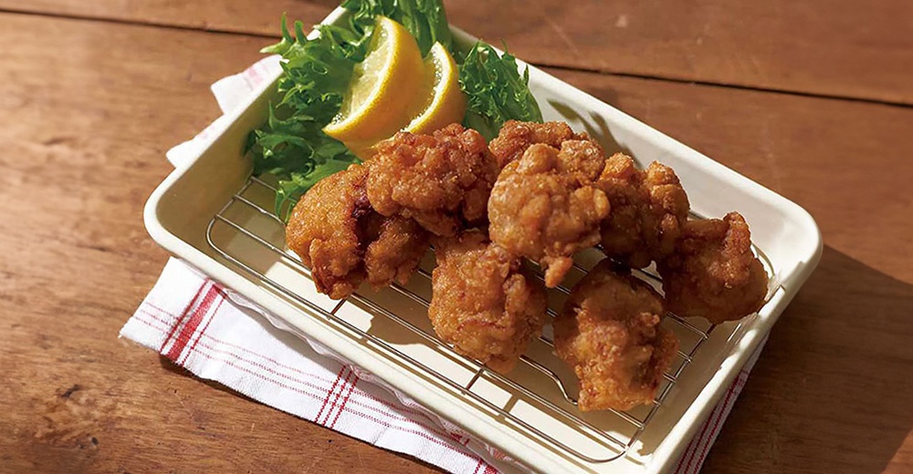 美濃燒釉彩萬用長方烤盤，內含烤雞塊、生菜及檸檬片，烤盤為淺米色，搭配銀色金屬網架，置於木質桌面，下方墊有紅白色格紋餐巾。