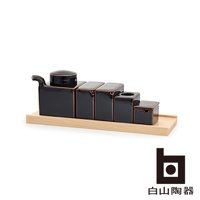 黑色陶瓷調味五件組，包含一個帶蓋醬料壺、三個方形調味罐、一個帶孔調味罐，以及一個帶抽屜的小方罐，整體呈階梯狀排列於淺色木盤上。