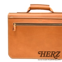 淺棕色皮革製成的手提包，帶有頂部提把、正面拉鍊口袋和白色縫線。