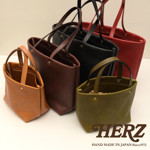 職人手作皮革托特包，展示多種顏色，包含駝色、深棕色、黑色、紅色及橄欖綠。包款設計簡約，以皮革材質製作，具有雙提把及四個內袋，適合日常攜帶。