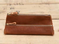 兩個棕色皮革製成的三角收納筆袋，帶有金色拉鍊和皮革拉環，其中一個較大，另一個較小，皆放置於木紋背景上。