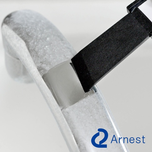 銀色金屬材質的彎曲物體，表面有細小的顆粒，一個黑色方形刮刀正從側面插入物體內的溝槽。