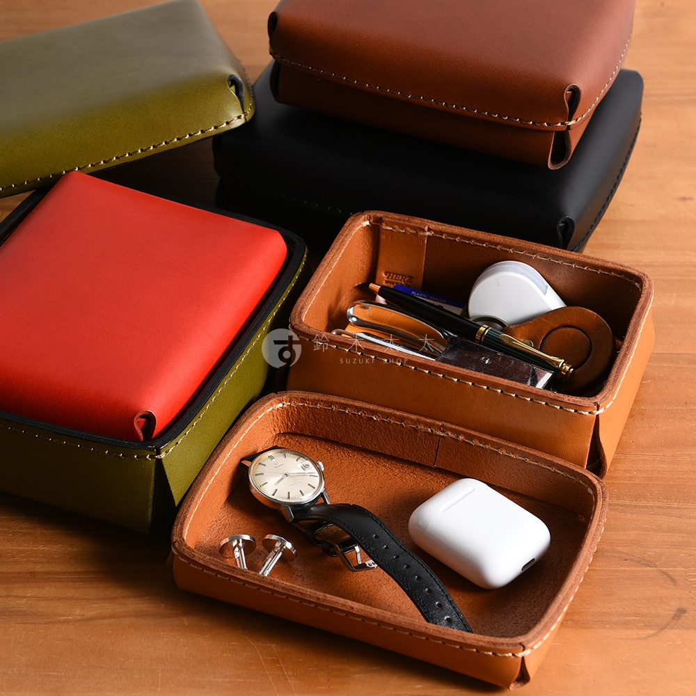 職人手作皮革小物收納盒，展示了多個皮革收納盒，包含紅色、橄欖綠、黑色和棕色。其中兩個棕色收納盒內分別放置了鋼筆、鑰匙圈、耳機、手錶和袖扣。