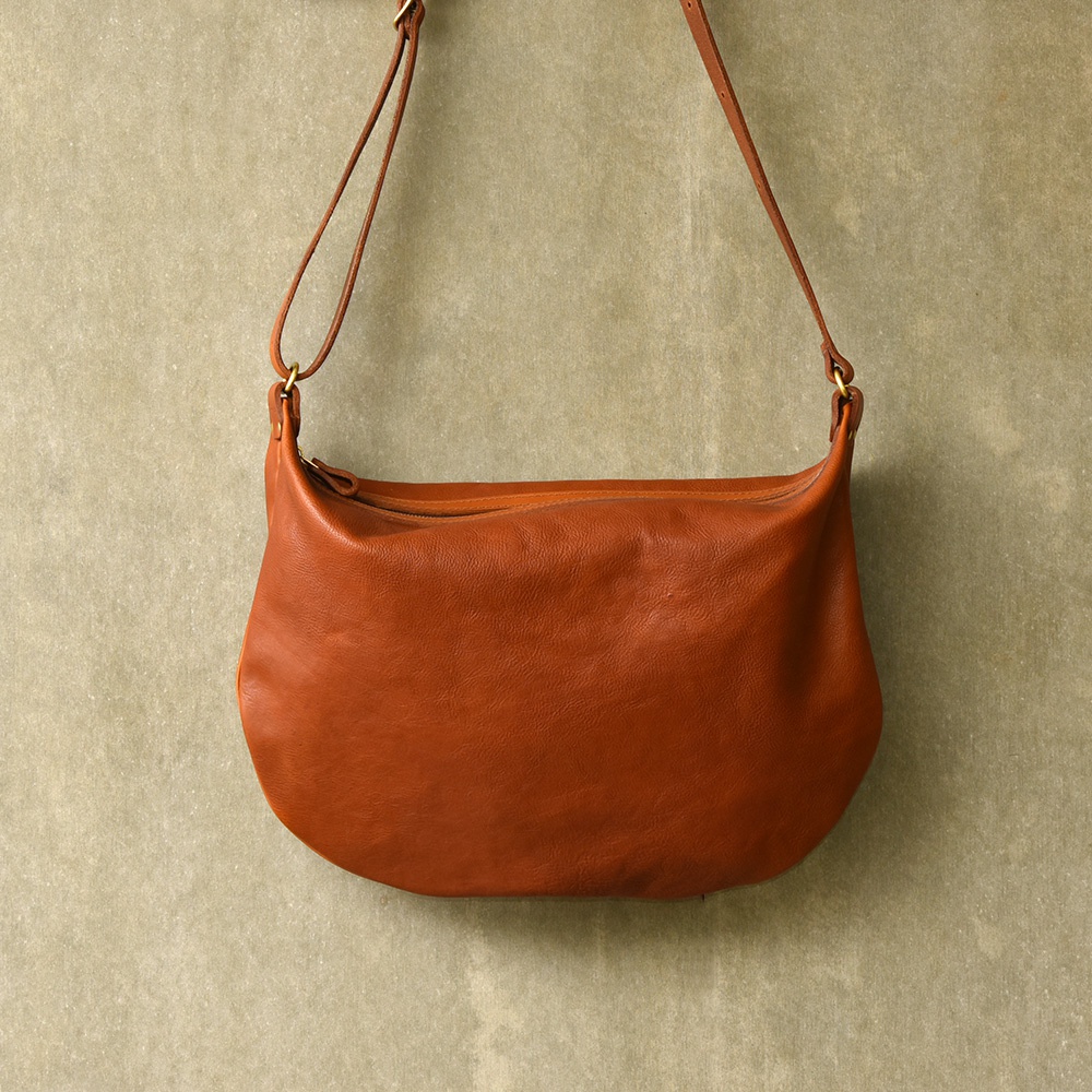 棕色皮革製成的單肩半月包，具有柔軟的質感和簡約的設計，並配有細長的肩帶。