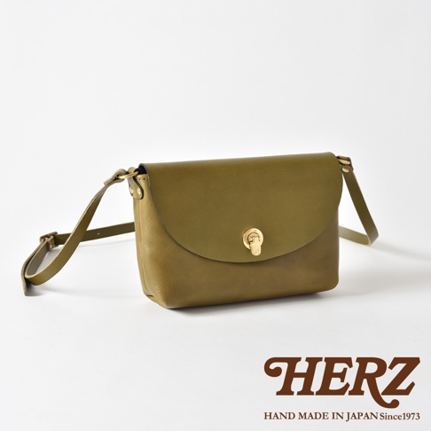 橄欖綠皮革迷你單肩手袋，翻蓋設計，配有金色金屬鎖扣和可調式皮革肩帶，整體呈現簡約復古風格。