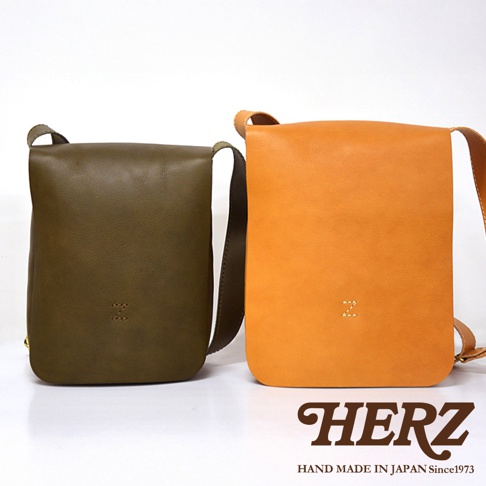 日本 HERZ 品牌，展示兩個職人手作皮革軟皮直式斜背包，一個為橄欖綠色，另一個為橘黃色，包包正面皆有品牌字母 Z 的壓印。