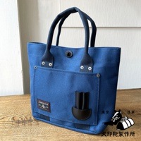 藍色帆布水桶托特包，設有深藍色織帶提把、外部貼袋和黑色皮革裝飾，袋身帶有品牌標籤。