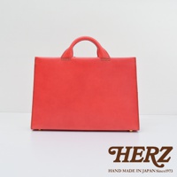 日本HERZ手工皮革紅色公事包，簡約方形設計，頂部設有雙提把，細節處縫線清晰可見，下方印有HERZ品牌標誌及「HAND MADE IN JAPAN Since1973」字樣。