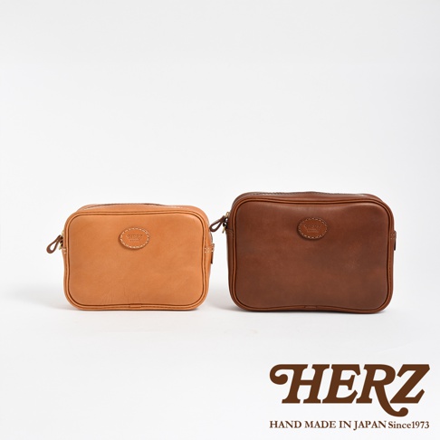 兩款職人手作皮革萬用手提包，分別為淺棕色與深棕色，皆為方形設計，採用拉鍊開合，正面中央有品牌壓印標誌。