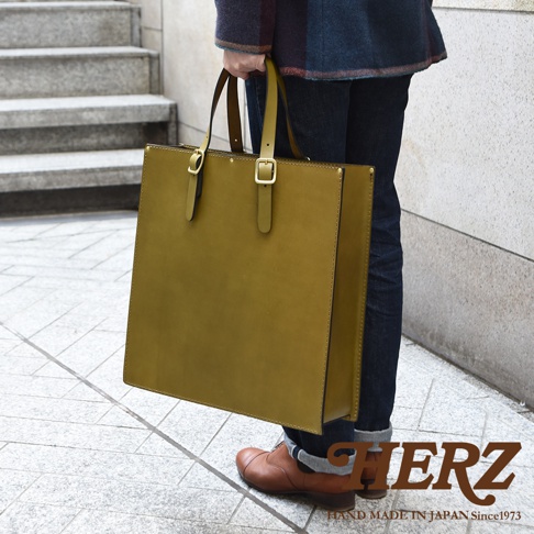 黃色皮革手提公事包，方形設計，有兩條皮革提把，提把上有金色釦環，包包側面有車縫線。