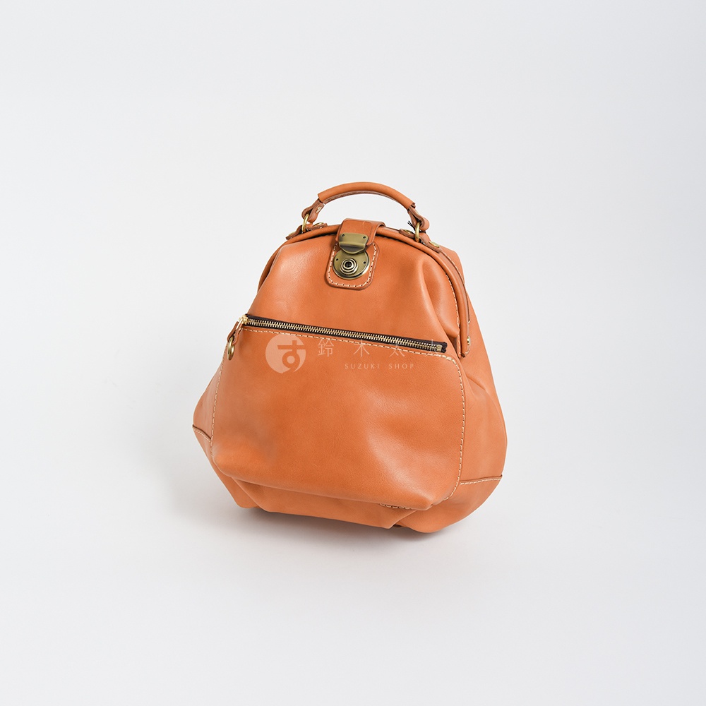 職人手作皮革輕旅行後背包 R-144，採用棕褐色皮革，設有金屬釦環、拉鍊外袋及縫線細節，造型經典復古。