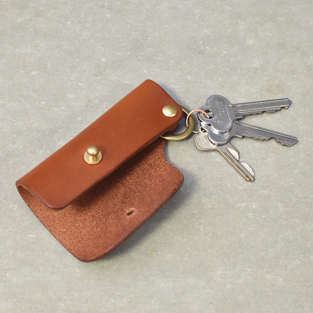 駝色職人手作皮革鑰匙套，附有銅色金屬按扣和鑰匙圈，圈上掛著三把銀色鑰匙。