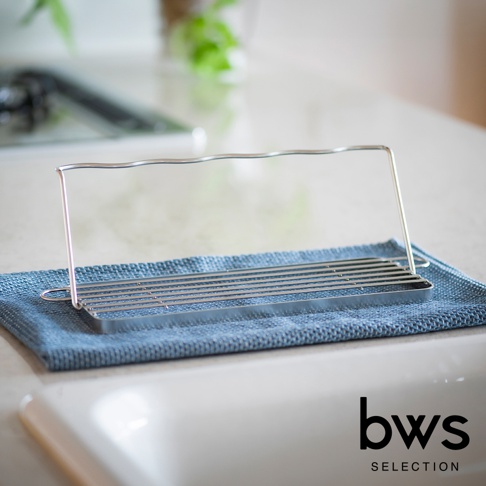 銀色不鏽鋼折疊杯壺瀝水架，置於藍色吸水布上，架面有數條平行金屬桿，頂部有波浪狀金屬支架，整體簡潔實用。