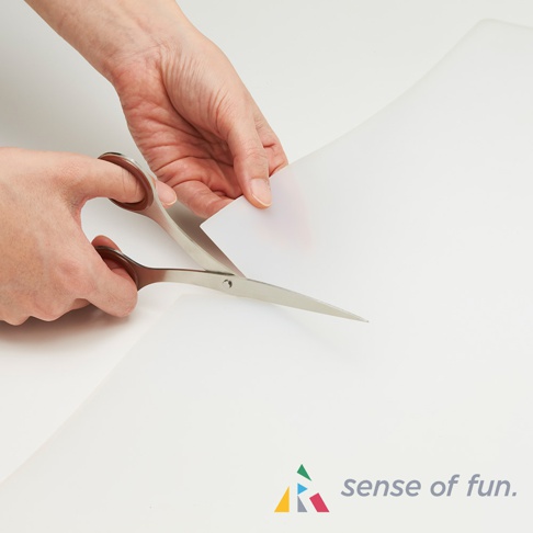 雙手持銀色剪刀，正在修剪一張半透明的白色耐高溫料理台保護墊。