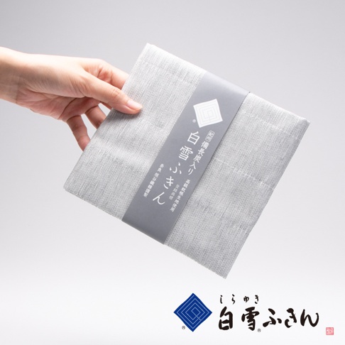 一隻手拿著一疊淺灰色、帶有織紋的家事拭巾，上面有灰色封套，印有日文文字與菱形圖案。