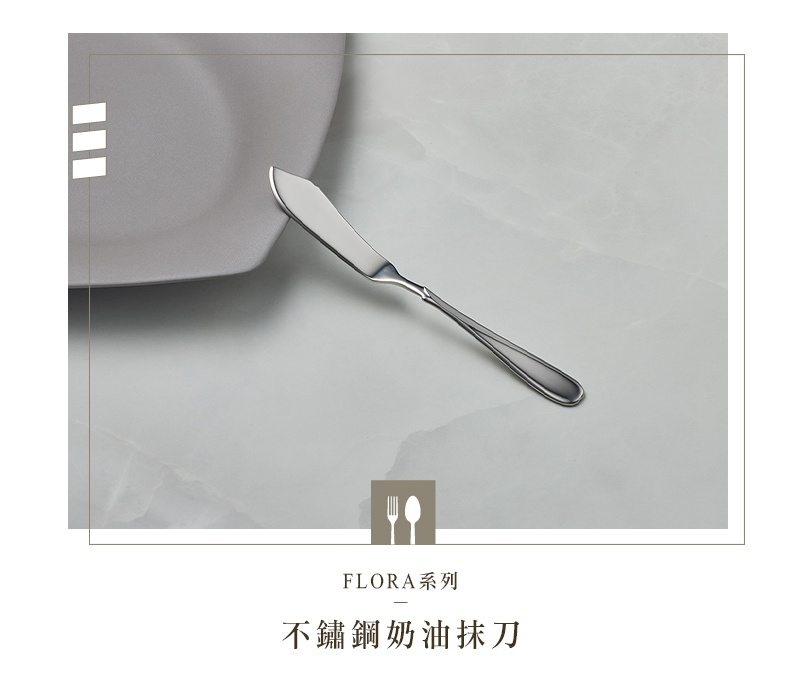 不鏽鋼奶油抹刀，刀刃呈彎月狀，手柄處有細緻的紋路裝飾，置於淺灰色盤子旁。