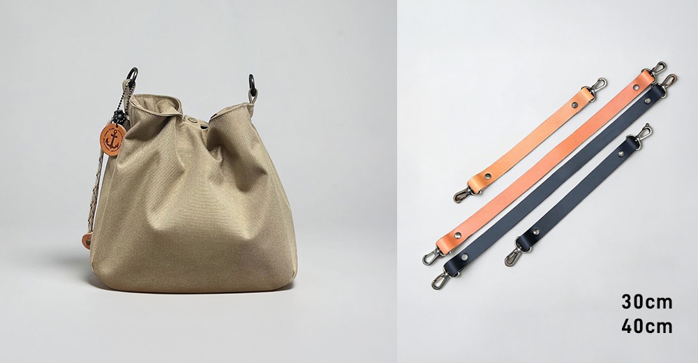 左側展示一款卡其色防潑水手提包，包身圓潤簡約並附有船錨圖案掛飾，右側則陳列兩款長度分別為30公分與40公分的皮革提把，包含淺棕色與深藍色兩種款式，均配有金屬扣環。