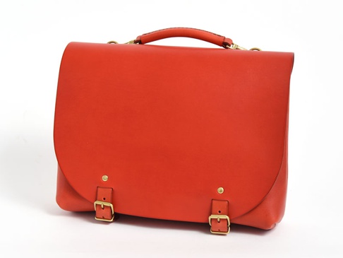 橘紅色皮革製成的職人手作雙扣兩用側背包，具有提把、可調節長度的肩帶連接環，以及兩個金屬釦環和鉚釘，風格簡約。