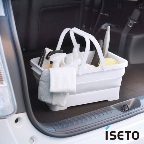 白色伸縮提籃裝有清潔用品，包括噴瓶、刷子和擦拭布，提籃有兩個白色提把，置於汽車後車廂內。
