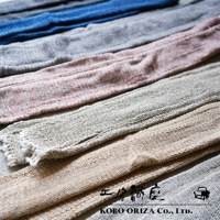 排成一列的 MOJIRI NECK’ｍ 輕柔有機棉遮陽袖套，呈現藍色、淺灰色、粉紅色混紡、淺棕色和深灰色等不同顏色。材質為輕薄的編織有機棉，觸感柔軟，部分袖套的末端帶有流蘇。