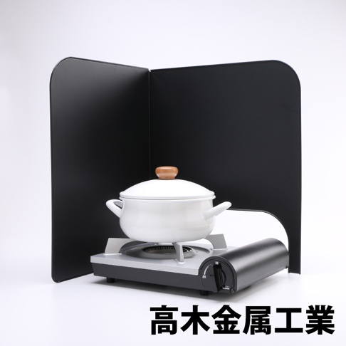 黑色 L 型折疊擋油板，兩塊面板以直角連接，中間放置一個帶木質鍋蓋把手的白色鍋具，鍋具置於灰色與黑色相間的爐具上。