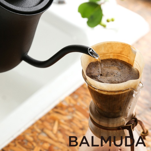 黑色手沖壺正將水注入裝有咖啡粉的濾紙杯中，水流細長，展現手沖咖啡的過程。