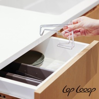 手持一個銀色伸縮式不鏽鋼砧板架，架子由金屬線條彎折而成，造型簡潔，可放置於抽屜內。