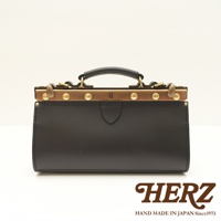 黑色皮革復古口金手提包，配有金屬鎖扣、黃銅色鑲邊和提把。包身有縫線裝飾，正面中央有一個盾牌形狀的皮革飾片。