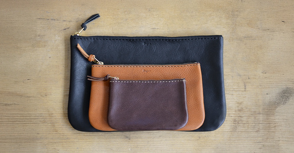 黑色、棕褐色和深棕色職人手作皮革Organ拉鍊式小物收納袋，三種尺寸疊放，特寫。