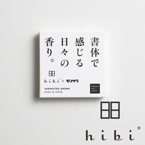 白色背景中央擺放著 hibi 與 Morisawa 聯名香氛火柴禮盒，正方形外盒印有書法字體日文標題，以及兩者的品牌標誌與 MADE IN JAPAN 字樣。右下角額外標示了 hibi 的圖示符號與品牌名稱。整體設計呈現簡約風格，強調文字與香氣的結合。