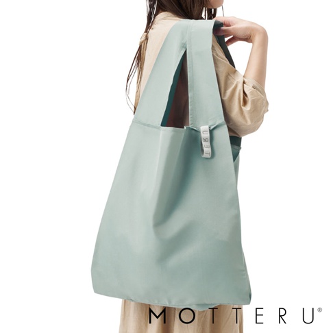 一位女性展示一個淺綠色的大容量摺疊環保隨行袋，袋子由輕巧的尼龍材質製成，具有寬提把和品牌標籤。