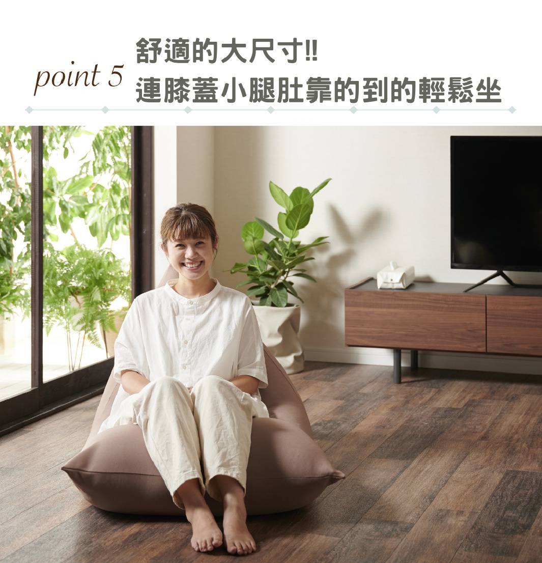 一位女士坐在一個淺棕色針織布款懶骨頭沙發上，沙發擺放在有木質地板的客廳中，背景還有植物和電視櫃。